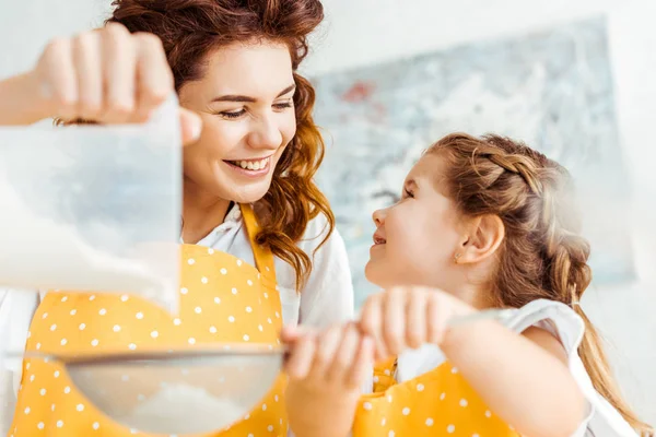 Selective focus of happy mother and daughter sieving flour together — Stock Photo
