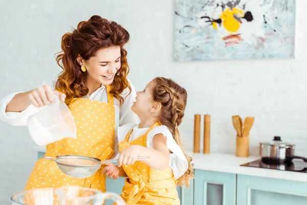 Selective focus of happy mother and daughter sieving flour together in kitchen — Stock Photo