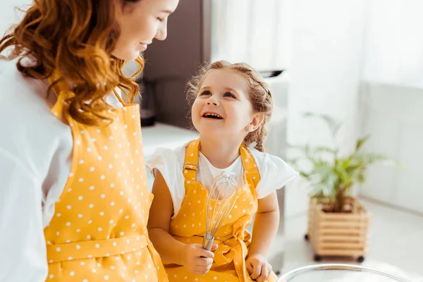 Mère souriante regardant fille heureuse avec ballon fouet — Photo de stock