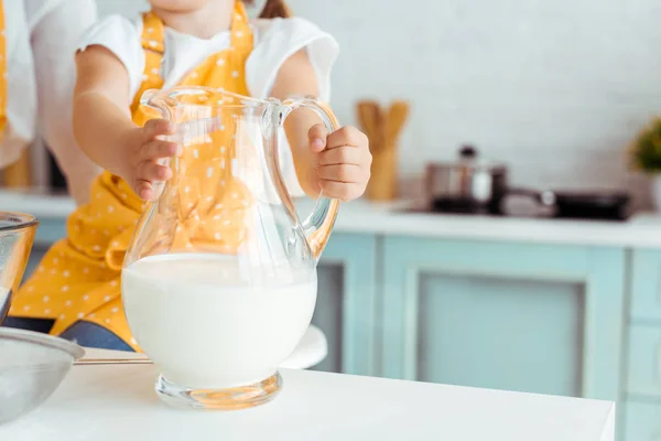 Cropped view of lid in apron holding glass jug with fresh milk — Stock Photo