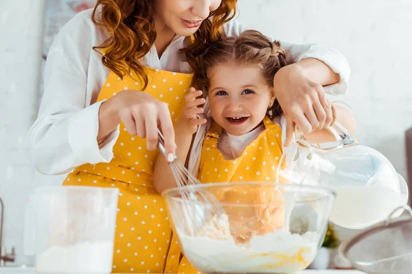 Madre e hija emocionada en delantales cocinando masa en la cocina - foto de stock