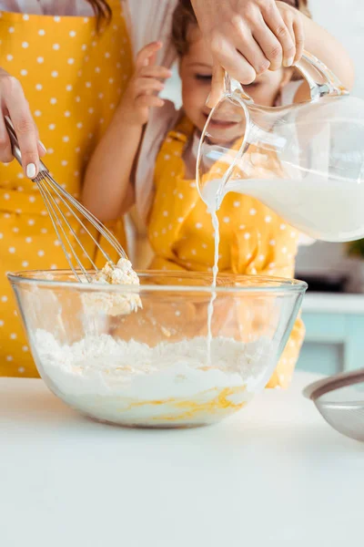 Enfoque selectivo de la madre ayudando a la hija emocionada en delantal preparando masa en la cocina — Stock Photo