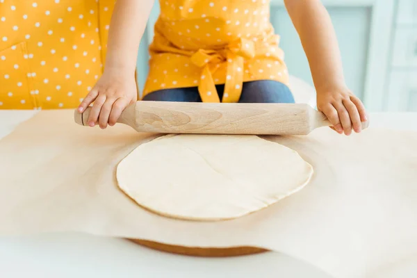 Cropped view of kid in yellow polka dot apron rolling out dough — Stock Photo