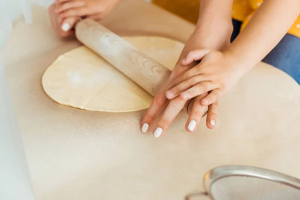 Teigansicht von Mutter und Tochter beim Ausrollen von Teig mit hölzernem Nudelholz auf Backpapier — Stockfoto