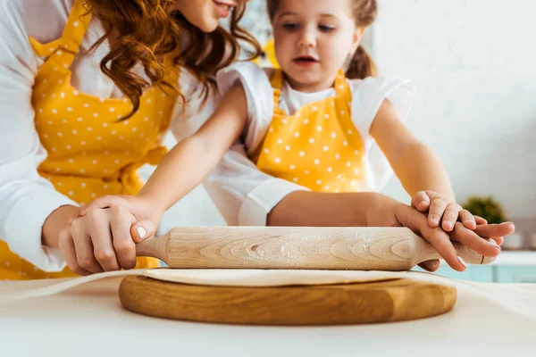 Selective focus of mother and daughter rolling out dough with wooden rolling pin on baking parchment paper — Stock Photo