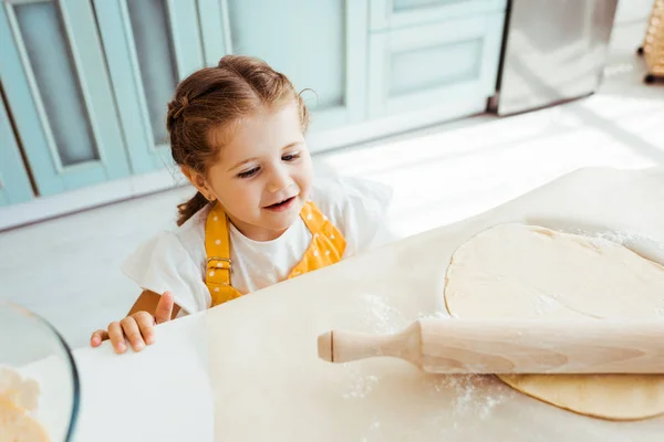 Aufgeregtes Kind betrachtet Teig mit Nudelholz auf Backpapier — Stockfoto