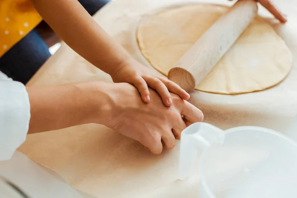 Cropped view of mother and daughter rolling out dough with wooden rolling pin together — Stock Photo