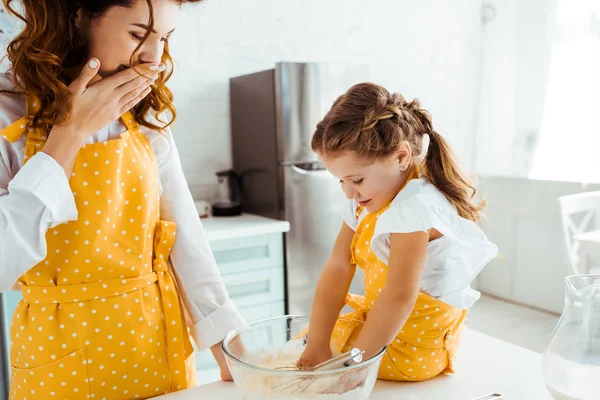 Schockierte Mutter schaut Tochter an, wie sie Hände in Schüssel mit Mehl legt — Stockfoto