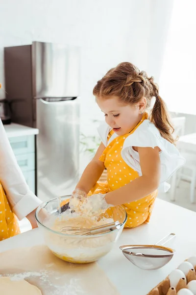 Excited kid in polka dot yellow apron mixing dough in bowl with hands — Stock Photo