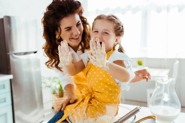 Sonriente madre mirando riendo hija con las manos sucias en la masa - foto de stock