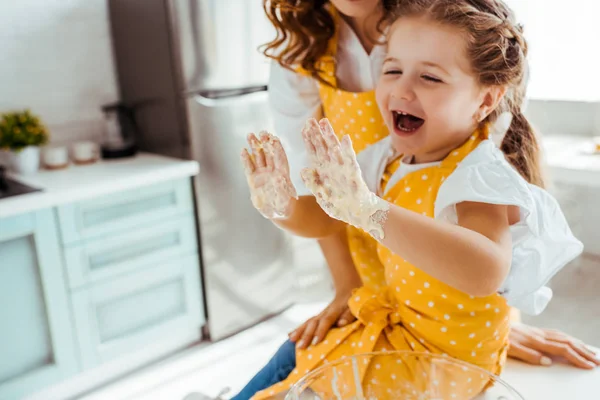 Happy excited child in polka dot apron looking at dough on hands — Stock Photo