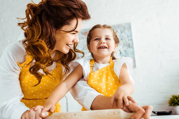 Happy mother with excited daughter holding wooden rolling pin together — Stock Photo