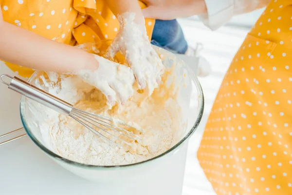 Cropped view of kid putting hands in bowl with raw dough and balloon whisk — Stock Photo