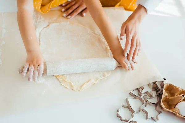 Top view of mother and daughter rolling out dough near dough molds on table — Stock Photo