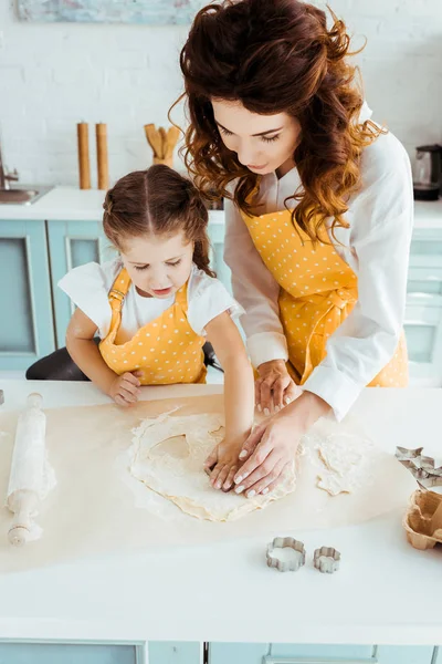 Madre e hija en delantales de lunares amarillos usando moldes de masa en la cocina - foto de stock