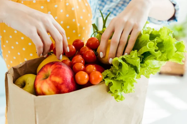 Partial view of woman touching fresh ripe fruits and vegetables in paper bag — Stock Photo