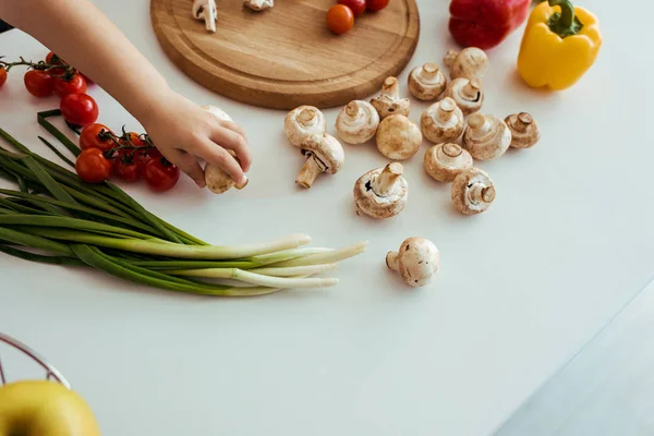 Vista parcial del niño sosteniendo el hongo en la mesa con verduras - foto de stock