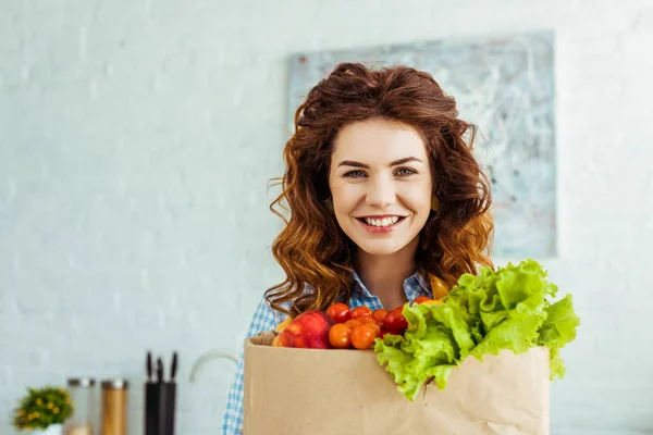 Sonriente hermosa mujer sosteniendo bolsa de papel con verduras frescas maduras - foto de stock