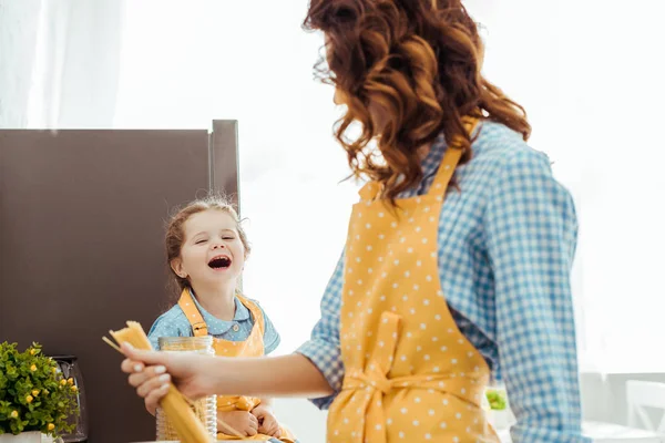 Selektiver Fokus der Mutter, die rohe Spaghetti in der Hand hält und aufgeregte Tochter betrachtet — Stockfoto