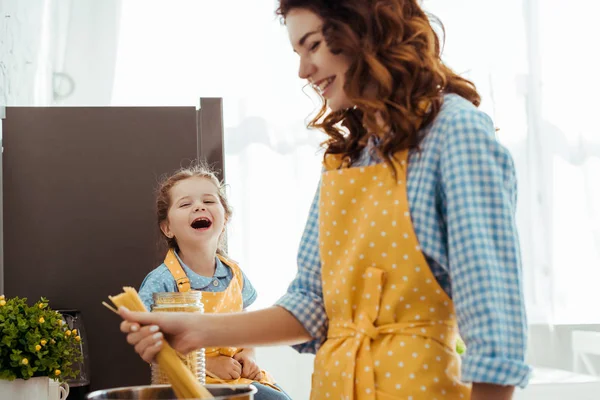 Sorrindo mãe segurando espaguete cru perto rindo filha animada — Fotografia de Stock