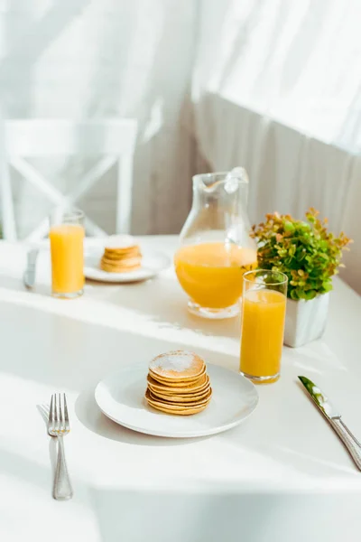 Foco seletivo de panquecas doces com suco de laranja fresco servido no café da manhã na mesa branca — Fotografia de Stock