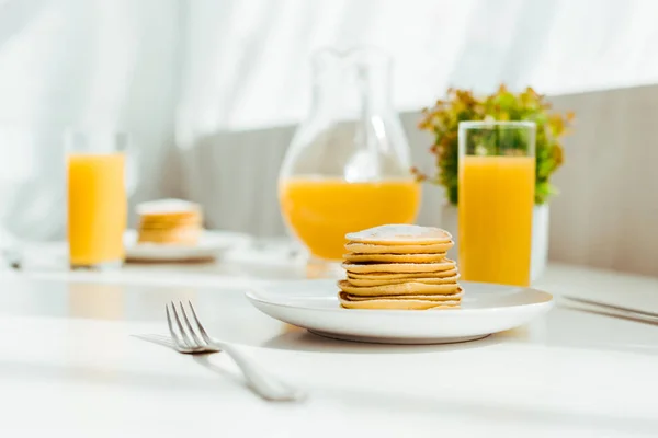 Selective focus of sweet pancakes with fresh orange juice in glass served for breakfast on white table — Stock Photo