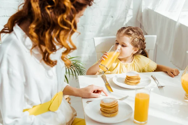 Enfoque selectivo de lindo niño bebiendo jugo de naranja mientras desayuna con la madre - foto de stock