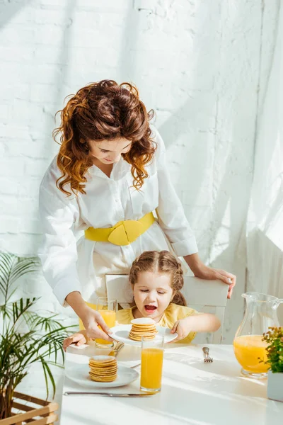 Mutter gibt aufgeregten Tochter Pfannkuchen zum Frühstück — Stockfoto