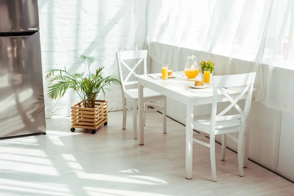 Interior of white kitchen with breakfast on table and sunshine — Stock Photo