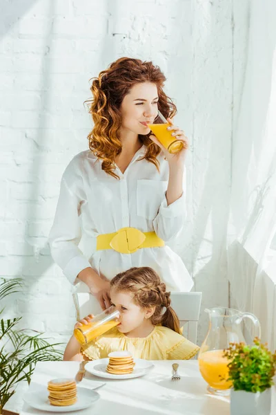Madre e hija bebiendo jugo de naranja mientras desayunan - foto de stock