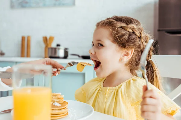 Selective focus of mother feeding daughter with pancakes — Stock Photo