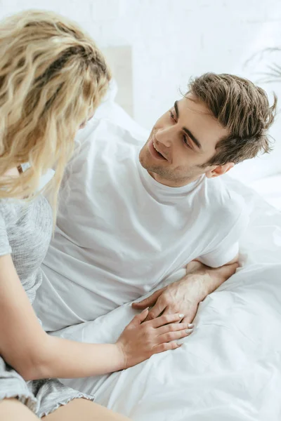 Handsome and cheerful man looking at blonde girl lying on bed — Stock Photo