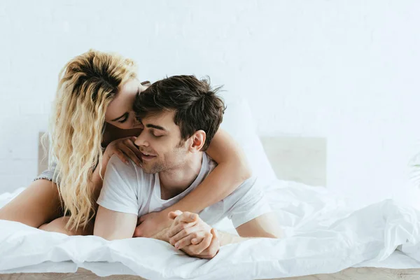 Happy blonde girl hugging handsome boyfriend lying on bed — Stock Photo
