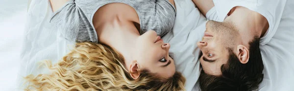 Panoramic shot of blonde woman looking at man while lying on bed — Stock Photo