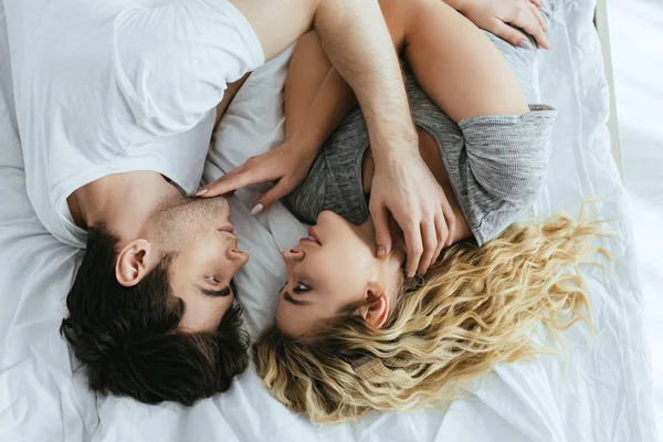 Vue de dessus de la jeune femme blonde touchant le visage du petit ami tout en étant couché sur le lit — Photo de stock