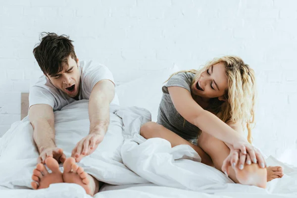 Atractiva mujer rubia y hombre guapo bostezando en la cama - foto de stock