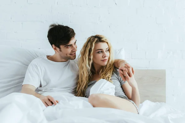 Homem feliz de mãos dadas com bela namorada enquanto deitado na cama — Fotografia de Stock
