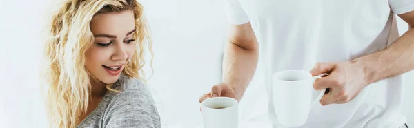 Colpo panoramico di uomo che tiene tazze con caffè vicino attraente donna bionda — Foto stock