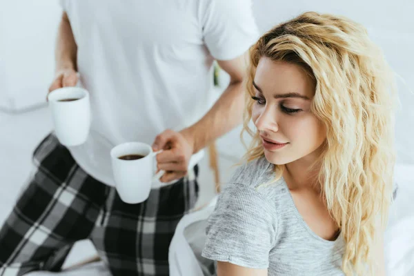 Vista cortada de homem segurando copos com café perto de mulher loira atraente — Fotografia de Stock