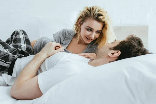 Веселая блондинка смотрит на парня лежащего на кровати — стоковое фото