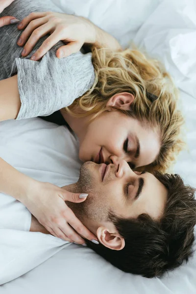 Happy blonde woman kissing boyfriend while lying on bed — Stock Photo