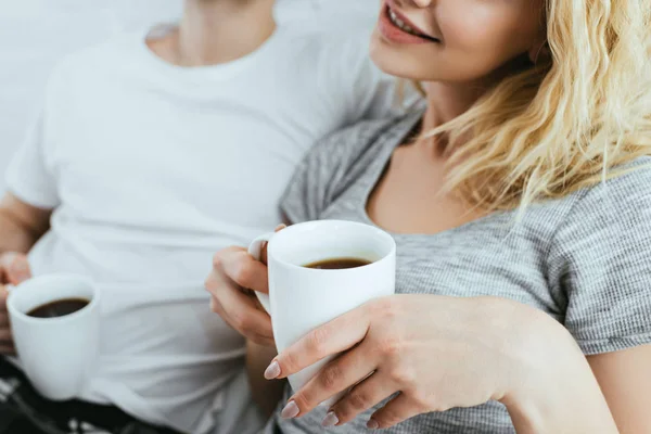 Vue recadrée de fille blonde heureuse tenant tasse près de l'homme — Photo de stock