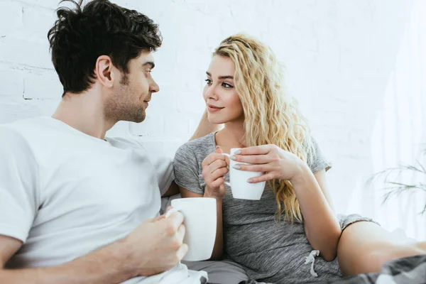 Feliz hombre guapo mirando atractiva rubia chica celebración taza - foto de stock