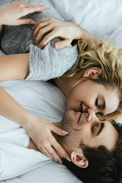 Cheerful blonde woman kissing boyfriend while lying on bed — Stock Photo