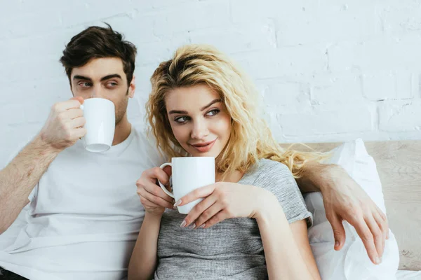 Веселая блондинка, сидящая с мужчиной и пьющая кофе — стоковое фото