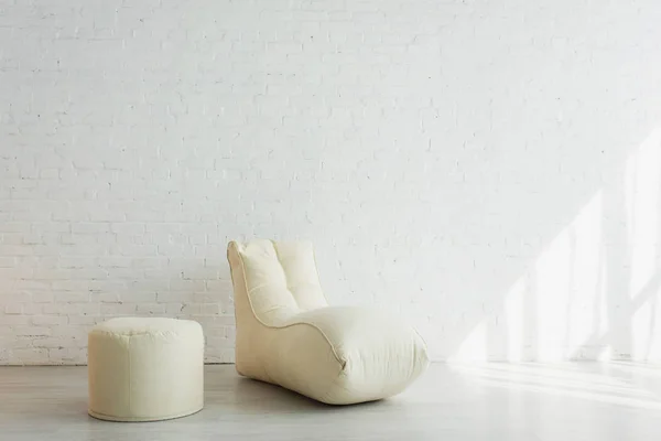 Cadeira de saco de feijão e pufe perto da parede de tijolo branco na casa moderna — Fotografia de Stock