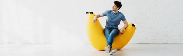 Tiro panorámico de hombre feliz sentado en la silla bolsa de frijol amarillo en casa - foto de stock