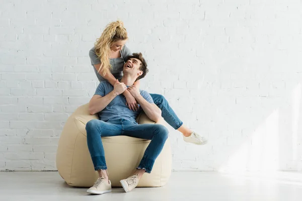 Gai blonde fille câlin heureux homme assis sur beige haricot sac chaise à la maison — Photo de stock