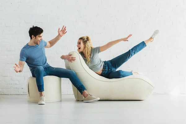 Cheerful girl looking at man while gesturing and lying on bean bag chairs — Stock Photo