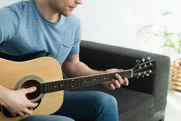 Cropped view of musician sitting on sofa and playing acoustic guitar at home — Stock Photo